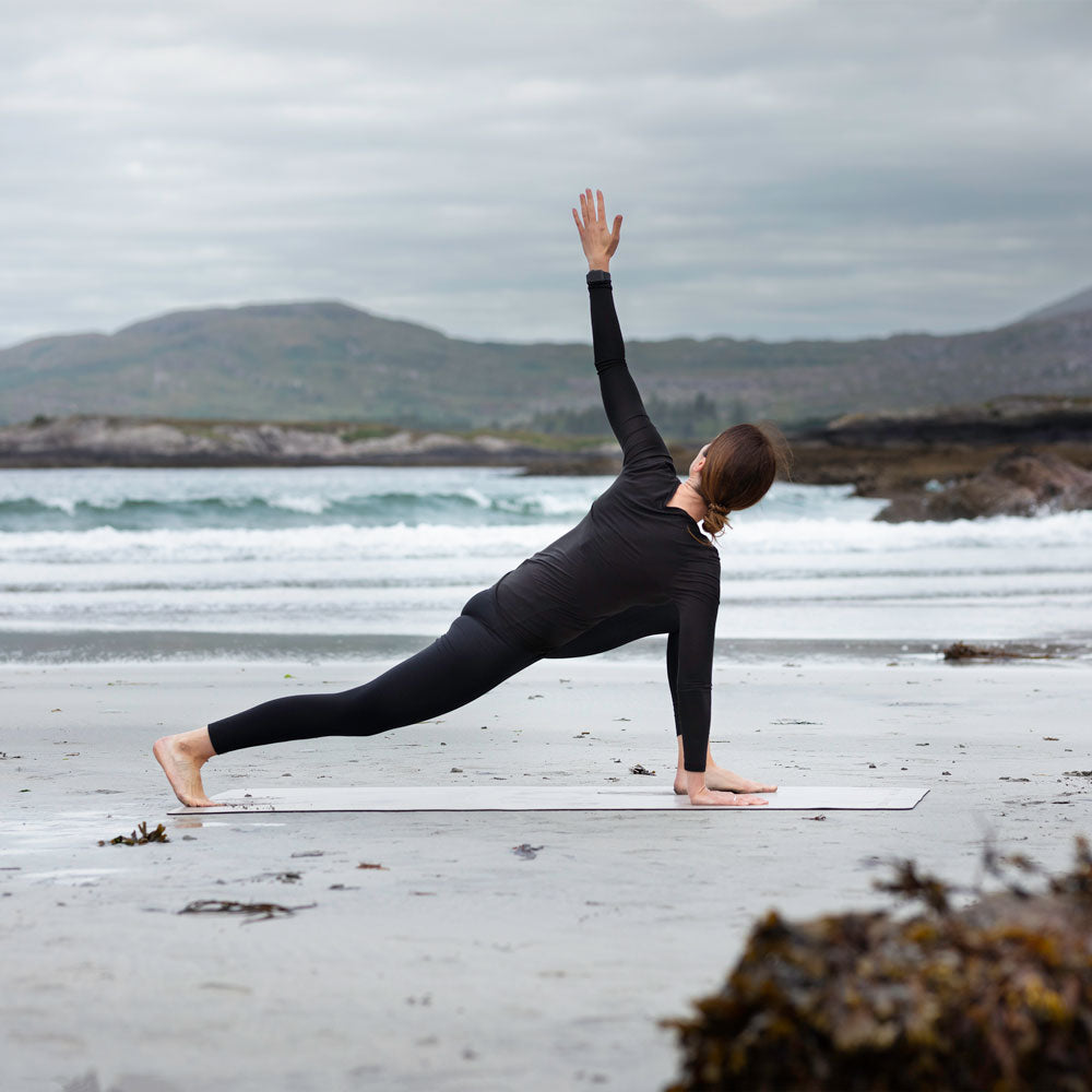 woman dressed in black top and leggings practicing yoga on an Inish Living exercise mat on the beach