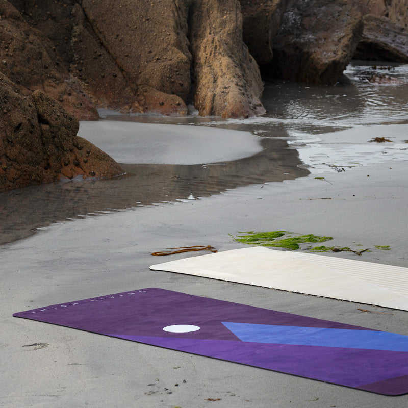 two Inish Living exercise mats laid out on a beach, to show durability, with rocks in background
