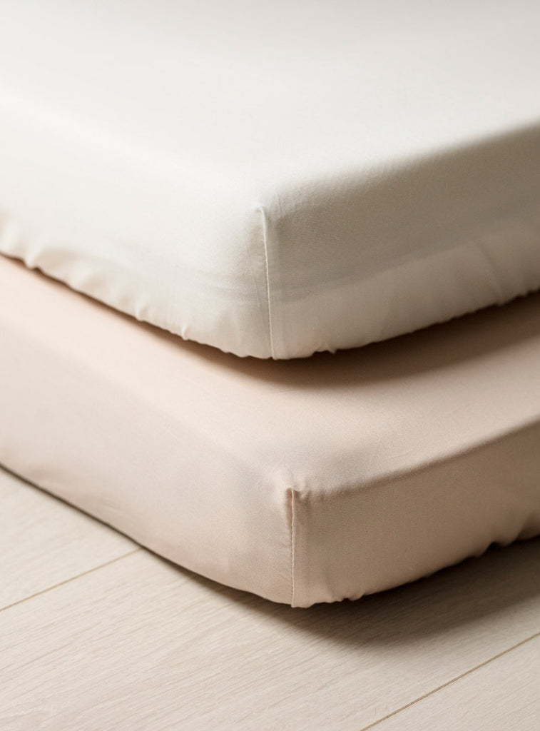 White fitted cot sheet on a baby's mattress. A second cot mattress has a fitted neutral sheet 