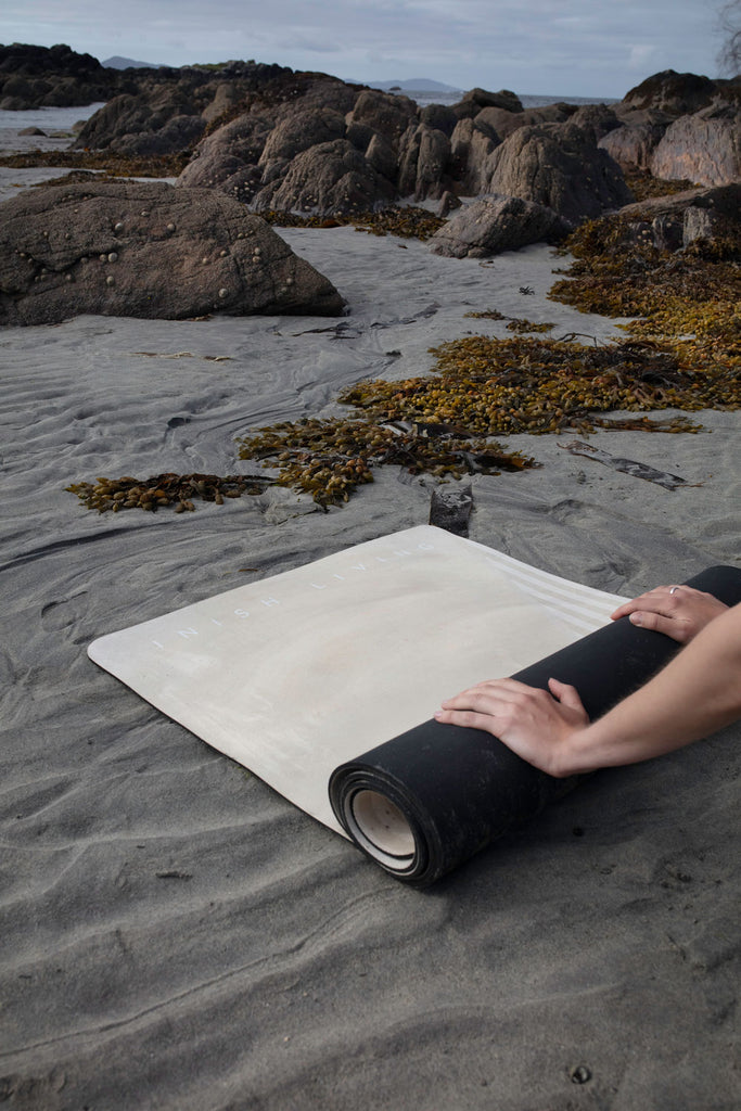 hands rolling up an Inish Living exercise mat on the beach