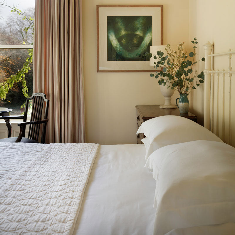 A bed made neatly in a clean bedroom with Stunning luxury bed linen from Inish Ireland. 