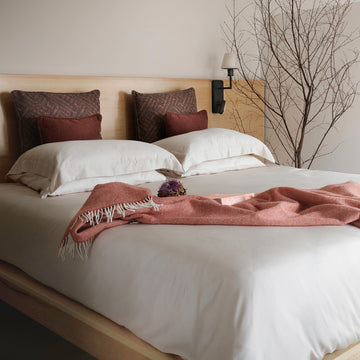 Luxury bed linen from Inish Living, based in southwest Ireland. Set up on a made bed with a blanket draped over it. 
