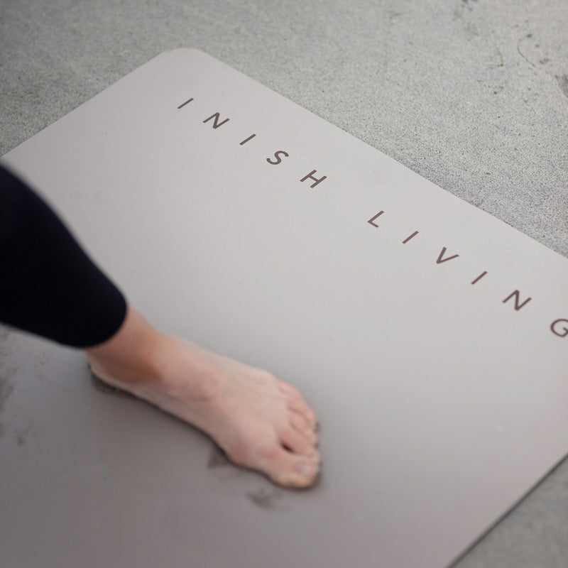 A foot shown using a grey high grip exercise mat on grey floorboarded floor