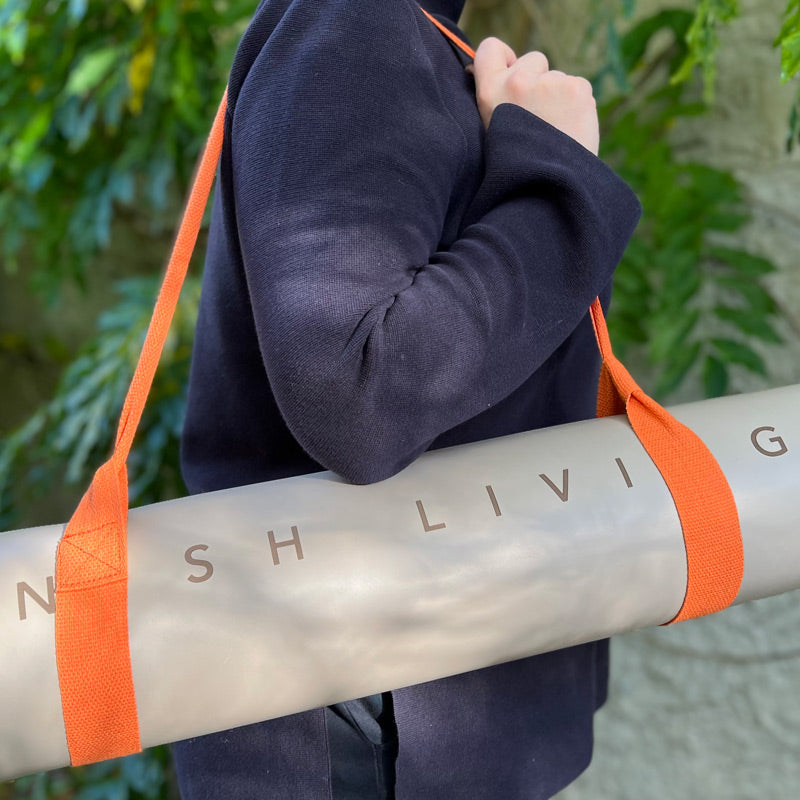 Person walks with a rolled up high grip Inish Living exercise mat with orange straps